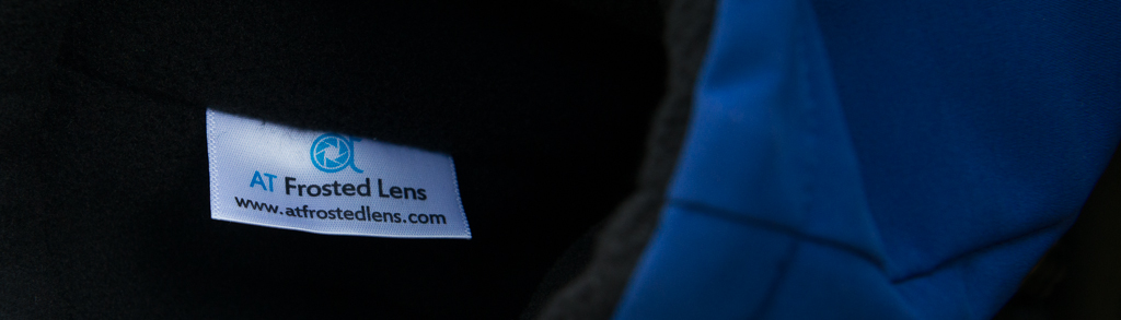Label inside a camera parka with AT Frosted Lens logo and website info.